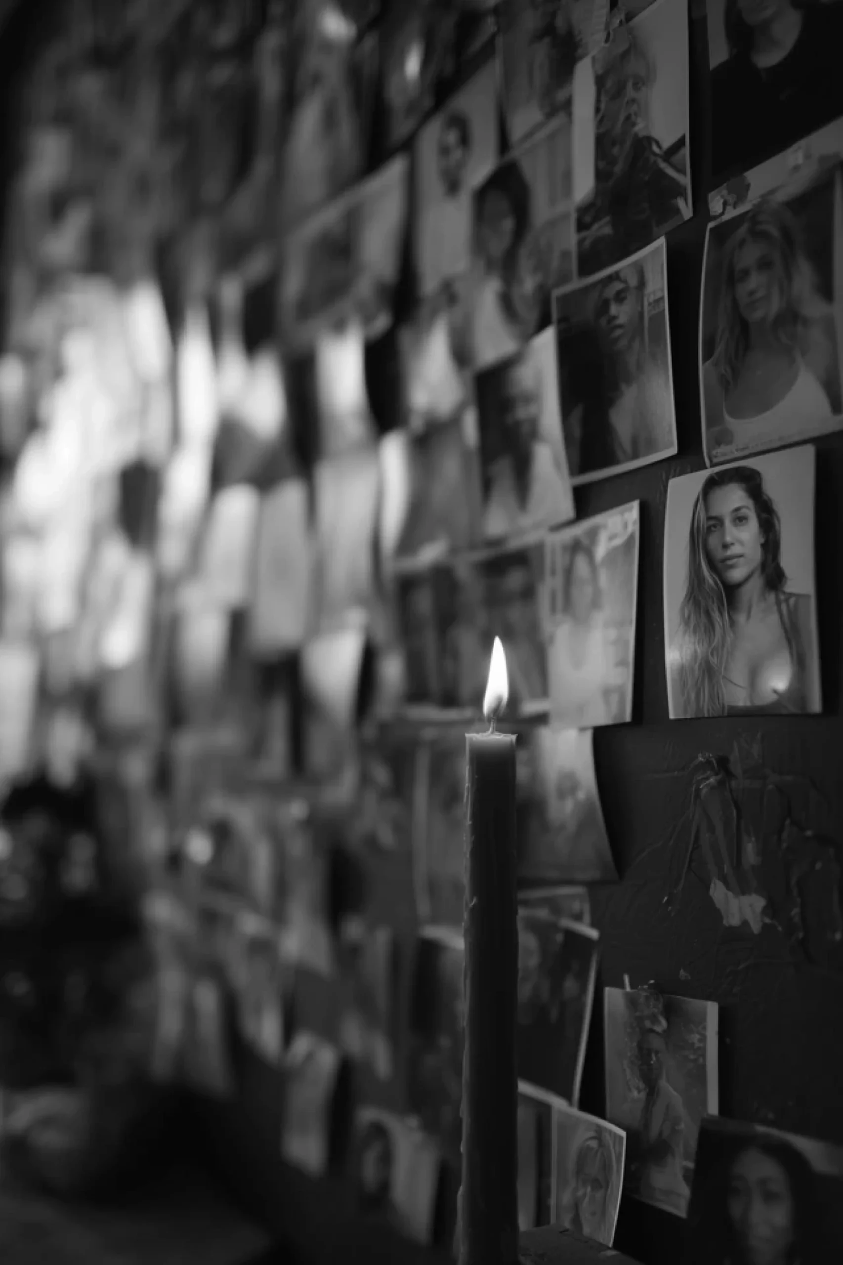 A lit candle stands in front of a wall adorned with various pictures, creating a warm and inviting atmosphere.