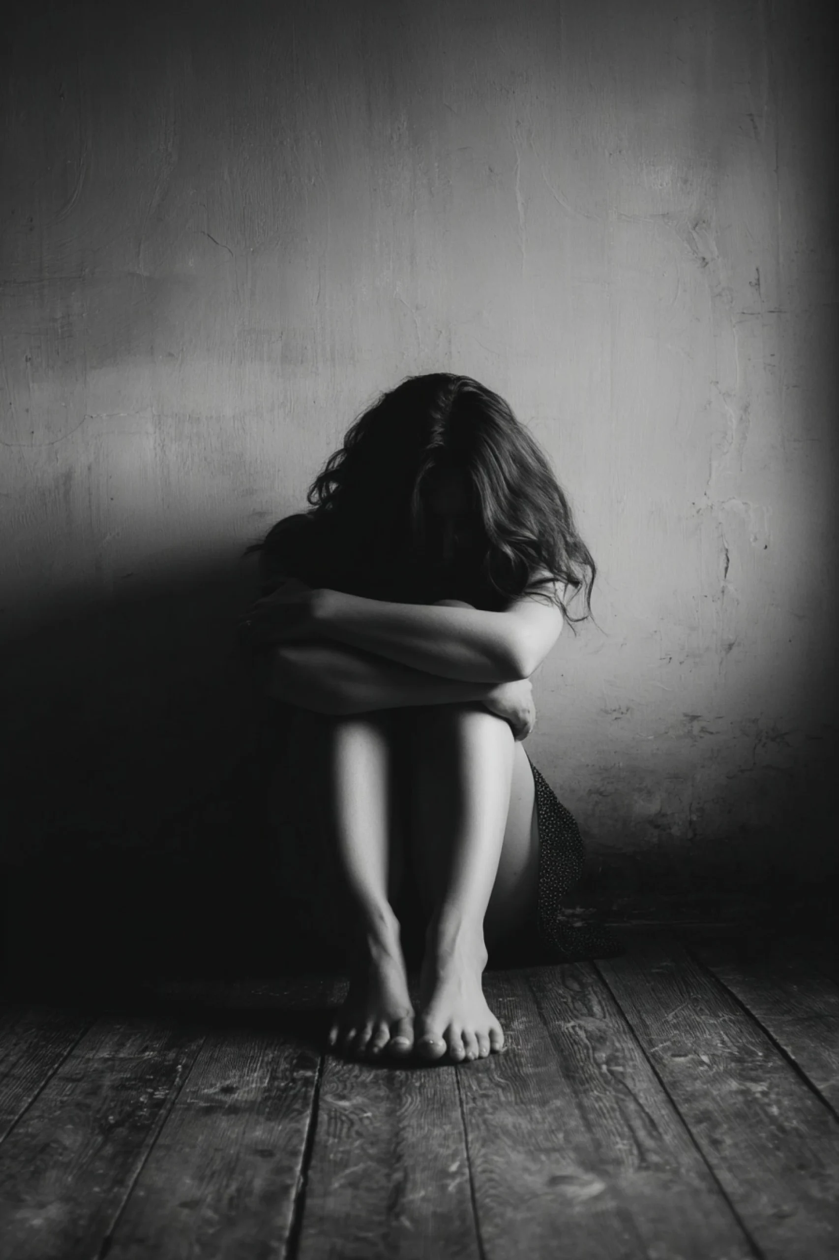 a woman sitting on the floor with her head down and arms around her knees